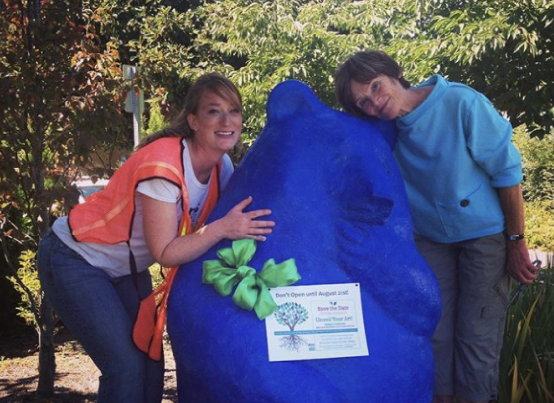 An image of Lori Goldstein and a friend standing outside by a large blue bear sculpture posing for the picture.